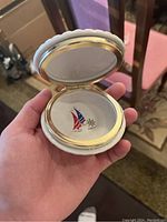 Porcelain container open showing inside lid with red and blue sailboat and ship's wheel design and gold trim.