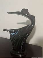 Black glossy porcelain abstract dancer statue in a dynamic pose, showing smooth, flowing lines.