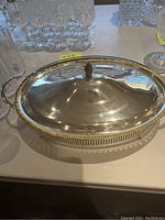 Photo of the silver plated serving dish with lid on a table, showing the oval shape, handles, and decorative rim.