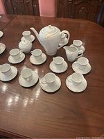 View of all 12 espresso cups with saucers arranged on table alongside teapot, milk jug, and sugar bowl.