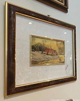 Framed winter scene painting showing houses with snow and frozen lake, signed by Lady Angela