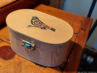 Closed oval bentwood cedar box showing top lid with First Nations sparrow bird design and brass latch closure.