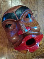 Top-down angled view of the carved wooden mask showing detailed face features, black-painted eyebrows, red painted lips, hollowed mouth opening.