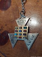 Close-up of front of pendant showing triangular shape, Hebrew inscriptions, and multicolored gemstones with one missing.
