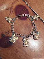 Photo showing gold-tone linked chain charm bracelet with five Disney character charms including Mickey, Minnie, Donald, Goofy, and Pluto, laid flat on wooden surface.
