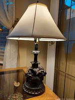Full view of the vintage copper lamp with cream fabric shade on a wooden furniture surface near a window.