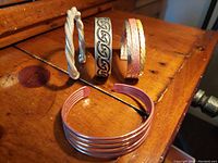 Four vintage handcrafted metal cuff bangles laid on wooden surface showing different designs and metal tones.