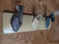 Photo showing entire mounted plaque with three animal heads: giraffe on left, cheetah in center, zebra on right, placed on wood floor.