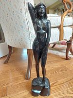 Full front view of vintage black lacquer nude wood statue showing detailed carving with arm raised behind head, standing on geometric base.