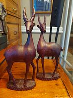 Two wood sculpted vintage folk art antelopes standing on a wooden surface, visible details of horns, body shape and base pattern