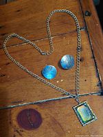 Photo showing vintage Pegasus round earrings and the rectangular Lord's Prayer pendant necklace on a wooden surface.