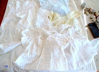 Group of five antique baby dresses in white and pale yellow shades, showing lace, ruffles, and pintuck designs, laid out on a surface.