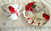 Cup and saucer placed next to a measuring tape showing regular cup size, cup on left with cardinal design and saucer on right with matching design