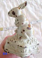 Side angle of a white painted cast iron bunny door stopper showing chipping paint and rust spots.