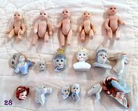 Top view of the entire lot showing five small ceramic doll bodies, multiple ceramic doll heads, busts, and animal figurine parts laid out on a white quilted surface.