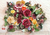Top-down view showing a large collection of mixed dark-colored porcelain rose pieces with attached greenery and smaller flowers scattered around. A ruler is included for scale showing pieces range roughly from 3 to 9 cm.