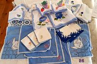 Photo of assorted vintage blue and white table linens including tablecloths, placemats, and embroidered napkins with fruit motifs.