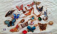 Wide view showing collection of butterfly-themed jewelry craft pieces including brooches, pendants, chain, and loose gemstones on white cloth background