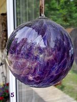 Front view of large purple swirling glass witches ball hanging against a window, showing its vibrant colors and swirled internal patterns.