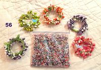 Top down photo showing five small floral wreaths made of faux pearls in green, orange, purple, lighter purple, and pink colors, surrounding a large zip seal bag filled with loose assorted colored faux pearl beads.
