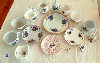 Top angle showing full set of purple floral china pieces including cups, plates, creamer, bowl, boot figurine, and candle snuffer