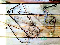 Set of three metal brackets with decorative scroll-style design. Shown laid out on wooden deck surface. The brackets vary in size with the largest approximately 18.5 inches in length. The metal shows signs of surface rust and wear.