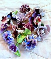 Wide shot of 15 porcelain rose heads in various purple shades with some green leaves on light background.