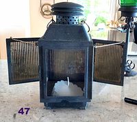 Grey speckled metal candle lantern with two side doors open showing white candle inside on a countertop with kitchen background.