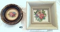 Two framed petit point cross stitch floral artworks on a white background. The round frame is dark with an ornate edge. The square frame is white and distressed.