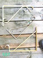 Three white metal shelf brackets laid on wood background, showing paint chipping and curled decorative ends.