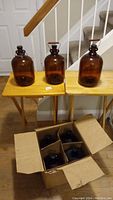 Three amber glass jugs with caps on two wooden tables; two have looped handles, one cracked handle