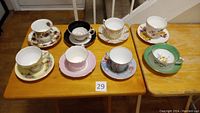 All eight bone china tea cups with matching saucers arranged on wooden tables, showing variety in patterns and colors.