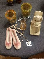Pair of pink ceramic ballet shoes with ribbons, two tall iridescent glass candle holders, a small clear pink glass vase, and a ceramic statue of a seated mother holding a child.
