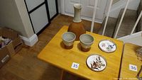 Photo showing the set of one carafe, two cups, and two floral coasters on wooden table near staircase.