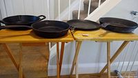 Four cast iron pans displayed on two folding tables, showing their size differences and condition.