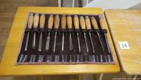Top-down view of twelve chisels neatly arranged in a brown leather roll-up case, showing wooden handles and metal blades of different sizes.