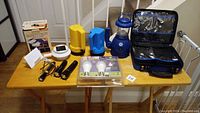 All items displayed on wooden table including flashlights, solar light, bulbs, lantern, and first aid case.