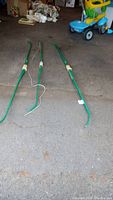 Photo showing three large green plastic bows laid on floor, two without strings and one with a white string attached. All have wooden style handles.