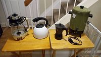 Full view of all four items on two wooden tables showing a large green Empire coffee maker, white stovetop kettle, Pezzetti espresso maker, and Eaton Viking glass coffee maker.