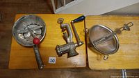 Overview of three kitchen tools: Spong meat grinder with blue handle, Passe-vite tool, and stainless steel food mill with red knob handle on wooden table.