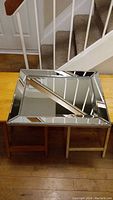 Mirror photographed resting on two small stools showing reflective beveled edged frame and central rectangular mirror surface.