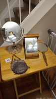 View of all four items on wooden table including two tabletop mirrors with bases, one hand mirror, and one metal clutch purse.