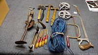Full view of assortment of old tools and coiled blue rope on carpeted floor