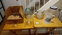 Overview of all items on wooden tables including glass jars, pitchers, teapot, and glass tea cups in a box