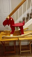 Side view of a wooden rocking moose toy with red painted body and natural wood rockers and antlers, showing the crack on the seat and some scratches.