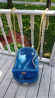 Blue Little Tikes toddler swing hanging from ropes, displayed on a wooden deck.
