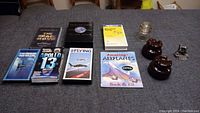 Photo showing various flight and space themed books, VHS tapes, a small coin, and decorative electric caps arranged on a surface