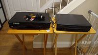 Two black VHS players on folding tables, with composite AV cables on top. One Sony and one Panasonic unit side by side.
