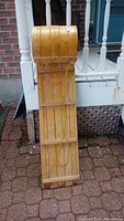 Front view of wooden sled laid flat on brick surface showing slatted wood design and attached green pulling rope.