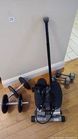 Image showing Sunny Health and Fitness step machine, adjustable weights bar with black weight plates, and 12 lb dumbbells against wall on wood floor.